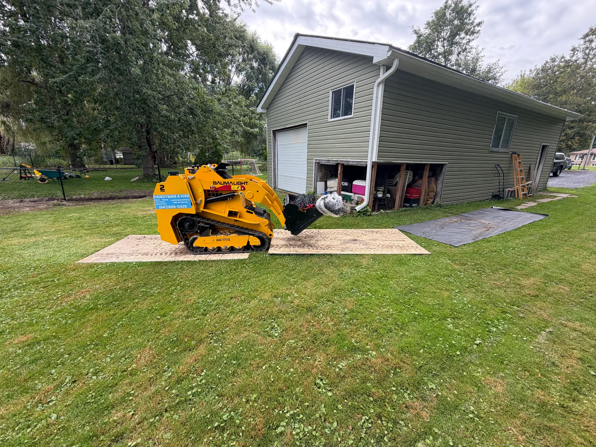 Track loader parked on plywood sheets laid across a customer's lawn